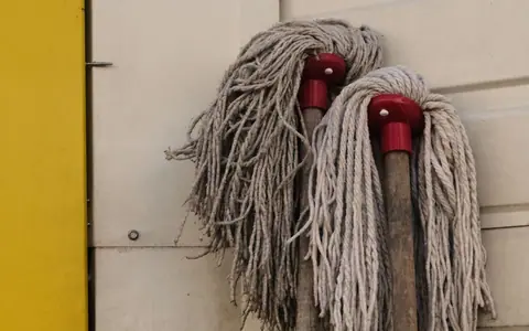 Two mop heads on wooden handles resting against a wall beside a yellow door.
