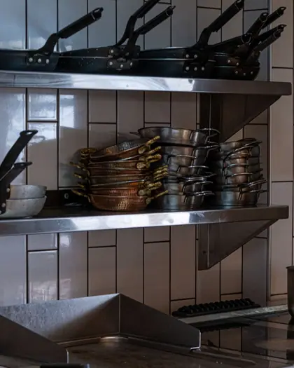 Pots and pans on commercial cooking equipment in a stainless-steel kitchen.
