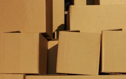 Plain corrugated cardboard cartons stacked in raking light.
